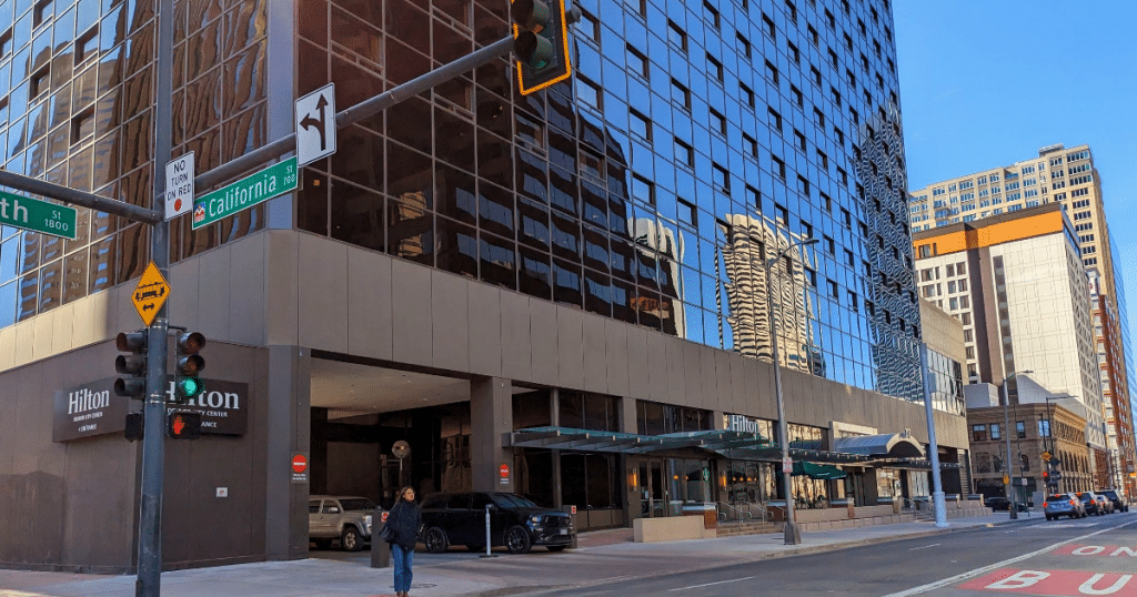 The Hilton Denver City Center Hotel stands proudly on the corner of California Street and 18th Street, its sophisticated facade illuminated by the warm morning sunlight.