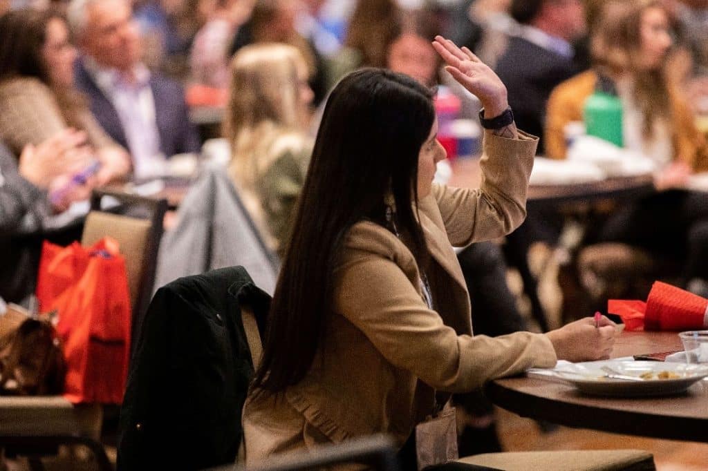 A young woman raising her hand and looking on in admiration as she receive valuable insights from experienced professionals during an inspiring day of learning