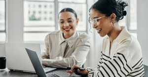 Two women reviewing a higher education website strategy on a computer in a collaborative workspace.